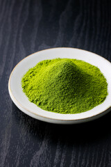 黒背景の木目に映える鮮やかな日本の抹茶パウダー　Vibrant Japanese matcha green tea powder on dark wood background