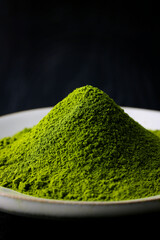 黒背景の木目に映える鮮やかな日本の抹茶パウダー　Vibrant Japanese matcha green tea powder on dark wood background