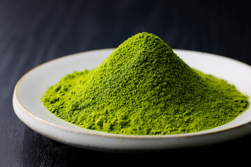 黒背景の木目に映える鮮やかな日本の抹茶パウダー　Vibrant Japanese matcha green tea powder on dark wood background