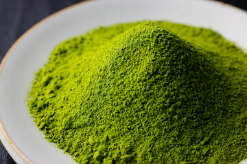 黒背景の木目に映える鮮やかな日本の抹茶パウダー　Vibrant Japanese matcha green tea powder on dark wood background