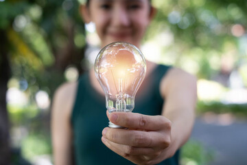 Smiling woman holding a glowing light bulb outdoors, symbolizing bright ideas, creativity, innovation, inspiration, energy efficiency, positive thinking, and future business or technology solution. © Bordinthorn