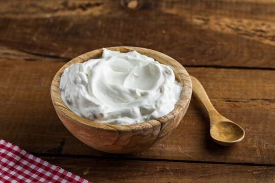 Plain greek yogurt in wooden bowl on wooden board
