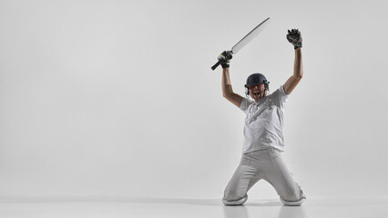 Fototapeta premium Cricket player celebrating victory on knees with bat raised in studio, shouting with excitement. Concept of championship win, sports achievement, tournament promotion, team success advertising.