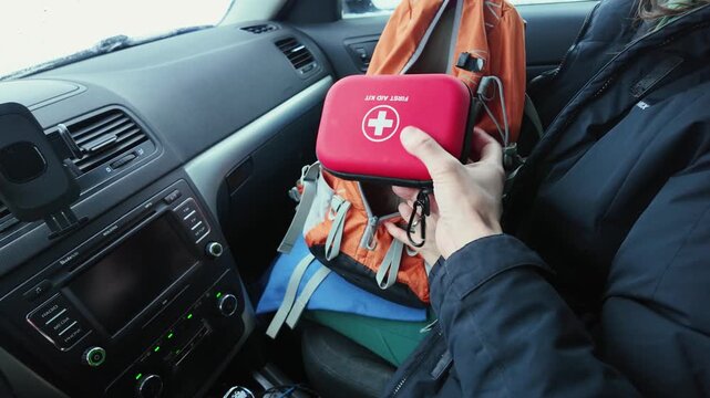 Driver Pulls Red First Aid Kit From Backpack On Passenger Seat Quick Sequence Of Hands Taking Pouch, Checking Zipper, Preparing Pouch For Stowage In Console, Tense But Controlled Mood, Snowy Daylight