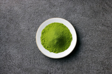 グレーのモダンな背景に映える鮮やかな日本の抹茶の粉末　Premium authentic Japanese matcha powder on a minimalist grey texture background
