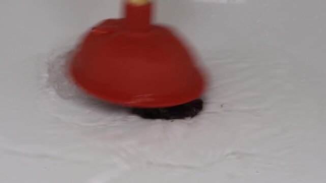 Unclogging a blocked bathtub drain with a plunger, hands in rubber gloves using a sink plunger to clear the drain hole, footage