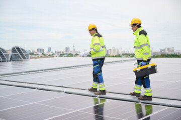 Two construction workers walking on a rooftop solar panel array, one carrying a blueprint, another with a toolbox. They wear safety gear, indicating a professional environment