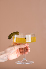 Cucumber pickle juice or brine in a glass with a pickled cucumber in a hand. Hangover drink. Vertical orientation.
