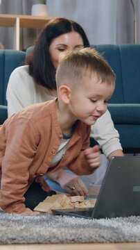 Portrait of charming positive carefree black-haired mom which spending free time with her small curious son at previsioning interesting cartoon on computer sitting on the fluffy carpet