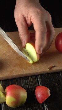Hand positioned with a knife, slicing through red appl on a wooden cutting board, revealing the fresh green interior of the fruit