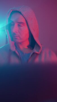 Focused Trader Monitors Fluctuations. Man With Hoodie Observes Realtime Trading Indicators. Man In Hoodie Scrutinizes Market Movements Rapidly Amidst Vibrant Neon Illumination And Tense Mood