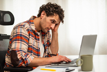 Tired and stressed young businessman using laptop while working from his home.	