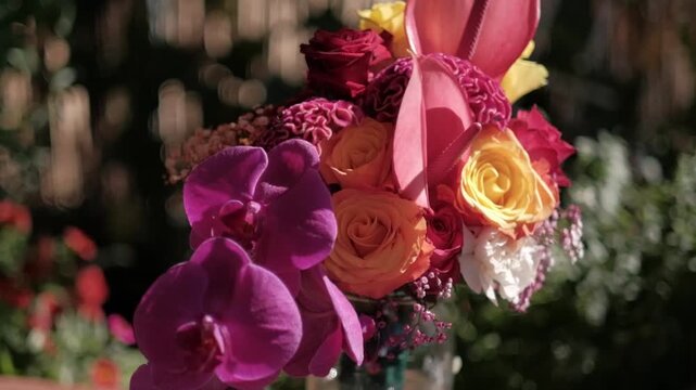 Vibrant floral bouquet featuring purple orchids, orange roses, and pink anthuriums in soft sunlight