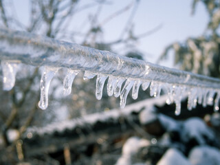 Detailed shot of a thick layer of ice and icicles on a metal wire against a blue sky.