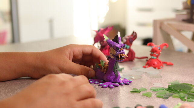 A close-up of a dragon-shaped craft made from air-blown plasticine with the addition of multi-colored glass pebbles and shells.