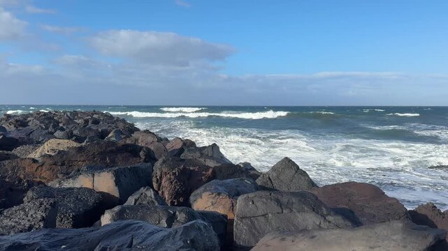 Rocky ocean coastline with breaking waves and blue sky, coastal landscape, ocean waves, rocky shore, blue sky, travel backdrop.