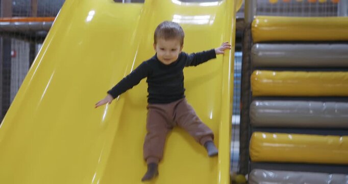 A boy slides down from children slide at a kids club, slow motion