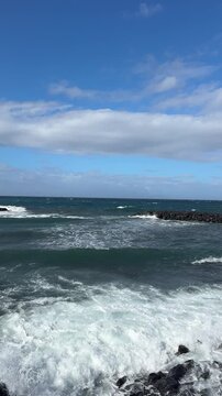 Rocky ocean coastline with breaking waves and blue sky, coastal landscape, ocean waves, rocky shore, blue sky, travel backdrop.