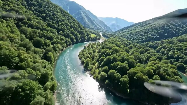 Aerial view captures a stunning serpentine river carving its path through a deep valley surrounded by lush dense green forested mountainsides under bright daylight.
