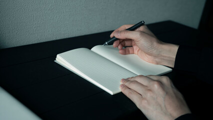 黒いデスクで方眼ノートにペンで書き込む手元 集中してメモを取るビジネスマン 思考の整理