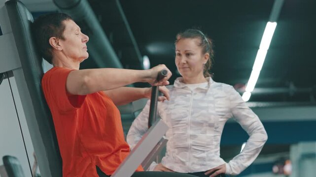 Senior woman working out on chest press machine with personal trainer
