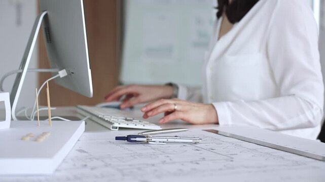 Architect creating new designs, working at a computer in office with blueprints and drafting tools. Business and architecture concept