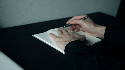 黒いデスクで方眼ノートにペンで書き込む手元 集中してメモを取るビジネスマン 思考の整理