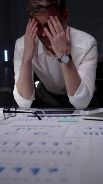 Stressed businessman suffering from overwhelming burnout and work overload, working late into the night, feeling frustrated with deadline pressure in a dark office environment