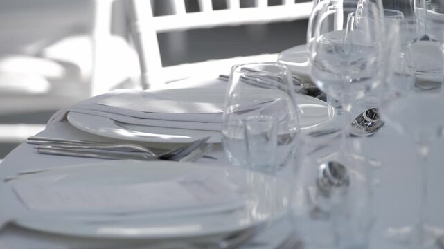 Close-up of a hand placing a white linen napkin onto a formal dinner plate as part of a table setting at an outdoor event
