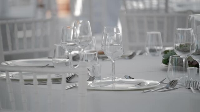 Elegant formal wedding table setting with white chairs, glassware, and silver cutlery