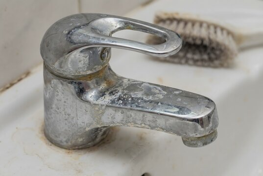 Close up macro texture of chrome bathroom faucet covered in white hard water limescale and mineral deposits