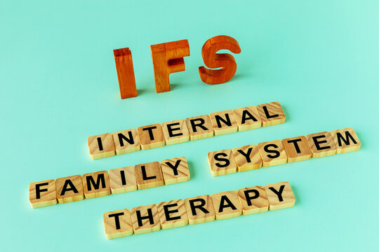 The acronym IFS and its individual words.  Internal Family Systems psychotherapy treatment concept. Standing wooden letters and letters painted on wooden blocks. Plain background.