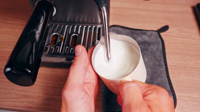 Top Down View of Hand Touching Metal Milk Pitcher to Check Temperature While Steaming Milk With Steam Wand Showing Barista Technique and Coffee Preparation Process