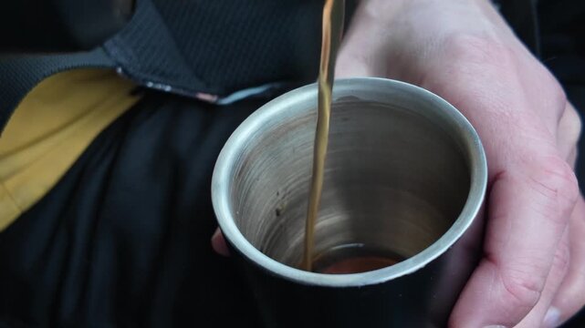 Cup Fills Calmly. Warm Drink Being Poured. Closeup Of Empty Metal Cup As Warm Liquid Fills It. Steady Stream Of Warm Brown Brew Flows Into Metal Cup Inside Car During Peaceful Morning