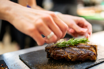 A chef meticulously places a fresh rosemary sprig onto a perfectly seared, juicy steak served on a rustic slate platter in a professional kitchen setting