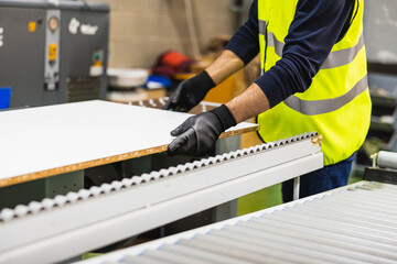 Fototapeta premium Worker handling wood panel on rollers in factory