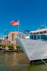 Fototapeta premium Close up of a white vessel's bow featuring the US flag with urban buildings in the background.