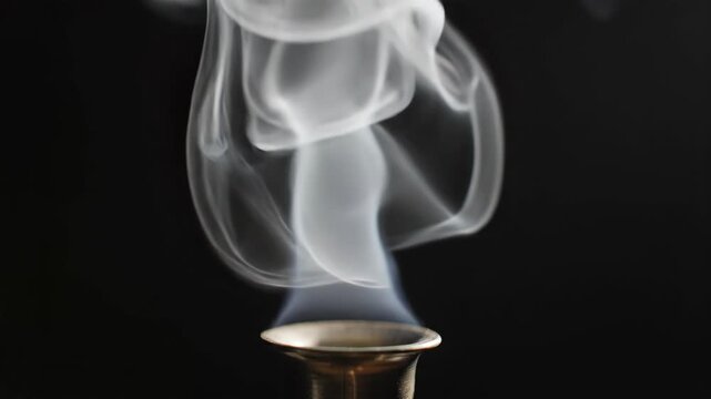 Ethereal smoke rising from metallic holder creating mesmerizing patterns. Smoke wafts gracefully into the air, bringing serenity and calm.