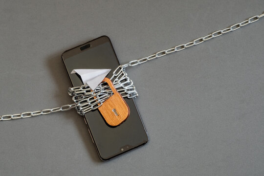 A smartphone wrapped in chains with a lock, data security and restricted digital access to online platforms, social media. No service. A broken phone. Calls, phone conversations, Telegram are blocked