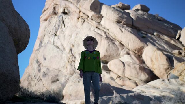A mature woman explores the desert trail in Joshua Tree National Park at sunset, discovering flora and rock formations during her hike.