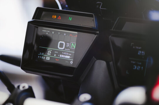 Detailed shot of a high-tech motorcycle cockpit featuring a dual digital LCD instrument cluster. Display shows speedometer, gear indicator, tachometer, ambient temperature , and trip information