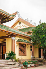 Fototapeta premium Vietnamese pagoda with traditional curved roof, yellow walls, and green tiles surrounded by greenery