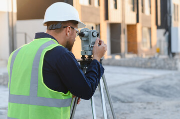 Surveyor using theodolite for land measurement at construction site