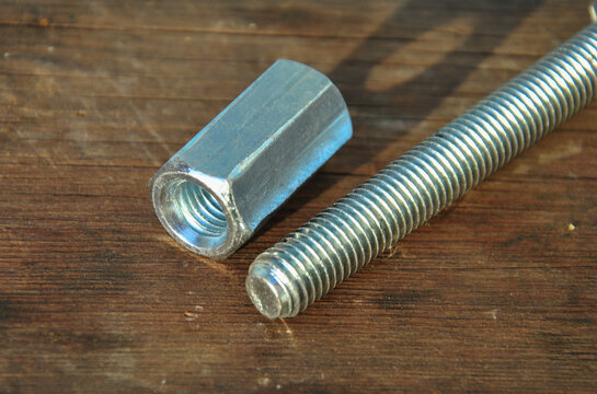 Long coupling nut and threaded bolt on a rustic wooden background.