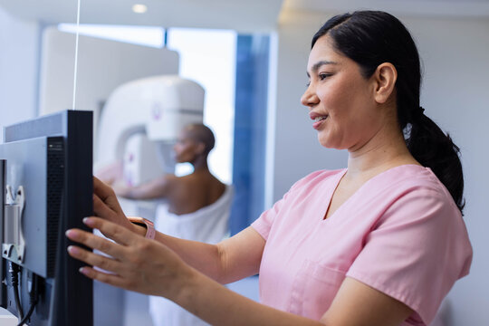 Asian tech adjusting controls in mammography-room, African-American patient positioning, copy space