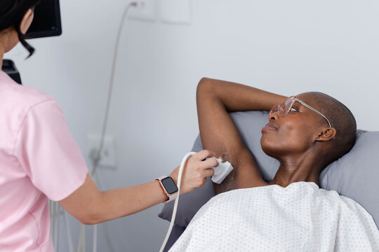Female African American patient and tech doing ultrasound using probe gel in exam room wearing gown