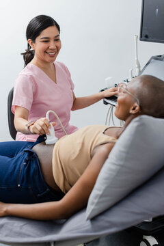 Female sonographer using probe on African American female patient with nasal cannula at exam table