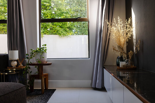 Large rectangular window is revealing green foliage in living room corner, curtains framing decor