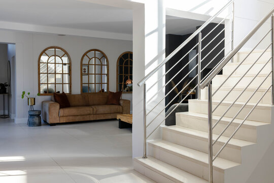 Stair flight is occupying right side, tan sofa and arched mirrors are anchoring left living area