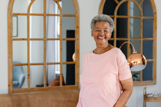Senior African American woman standing and smiling at home near arched wooden mirrors, copy space